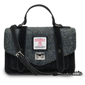 Islander suede satchel style handbag made with a black suede outer body and Black Herringbone Harris Tweed fabric. The synthetic leather and chain strap is draped over the bag.