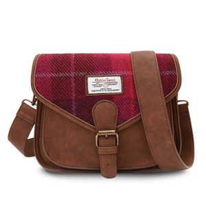 Harris tweed saddle style shoulder bag. You can see the dark brown synthetic leather, buckle closure and adjustable shoulder strap. The front of the bag is made from Harris Tweed which is in a fuschia, red and pink tartan pattern. On front of the bag is the Harris Tweed label of authenticity