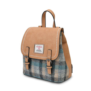 From the side the Islander Harris Tweed Jura Backpack in a blue and cream tartan design. It has a body of light tan faux leather and buckles on the front. 