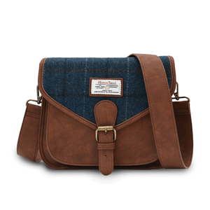 Harris tweed saddle style shoulder bag. You can see the dark brown synthetic leather, buckle closure and adjustable shoulder strap. The front of the bag is made from Harris Tweed which is in a navy check tartan pattern. On front of the bag is the Harris Tweed label of authenticity