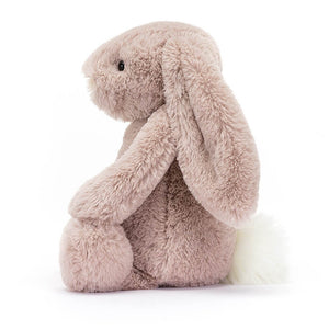 From the side the Jellycat Bashful Luxe Bunny Rosa with its legs sticking out in front and tail behind.