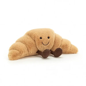 Jellycat Amuseable Croissant children’s soft toy in the shape of a pastry. It has golden drown fur all over its body and short chocolate legs sitting out front.