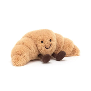 Jellycat Amuseable Croissant children’s soft toy in the shape of a pastry. It has golden drown fur all over its body and short chocolate legs sitting out front.