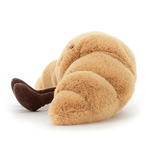 Jellycat Amuseable Croissant children’s soft toy from the side. It has little legs sitting out front.