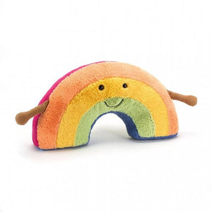 Jellycat Amuseable Rainbow children’s soft toy. He is made up of stripes of pastel colours from pink, yellow and green. He has a smile on his face and little brown corded arms at his side. 