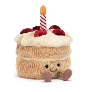 Jellycat amuseables birthday cake children’s soft toy. He has a great big smile, tiny little feet and wears a har of frosting strawberries and a candle on top. 