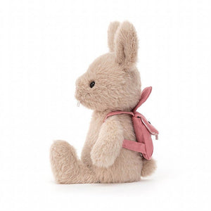Jellycat Backpack Bunny Rabbit children’s soft toy from the side. Her soft, fluffy legs are stretched out in front and she wears a pink backpack on her back. 