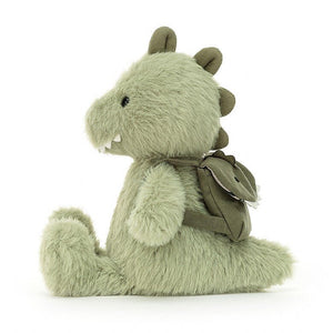 Side view of Jellycat Backpackers Dino green dinosaur children’s soft toy with his soft squishy legs sitting in front of him and backpack on his back. 