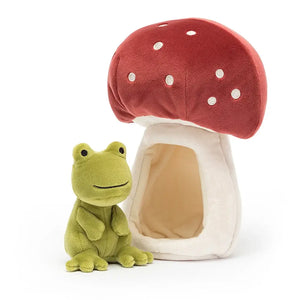 Jellycat Forest Fauna Frog children’s soft toy sits to the side of its read topped mushroom home. The soft toy can be removed from the home or placed inside. 