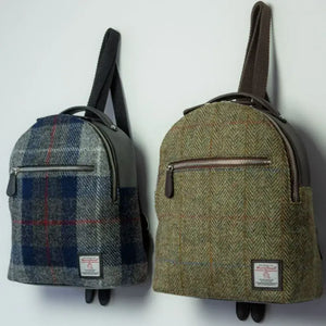 Two Harris Tweed Backpacks from Maccessori hanging on a wall. The one on the left is a grey and blue tartan and the one on the right a brown and green herringbone.