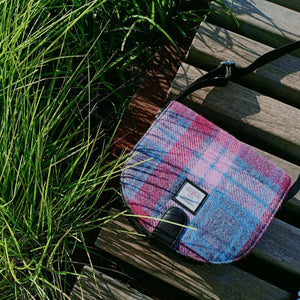 Pink and Blue Maccessori Harris Tweed Crossbody Bag sitting on a bench outside with its adjustable strap behind. 