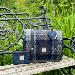 Harris tweed satchel in a blue and grey tartan sitting on a park bench. 