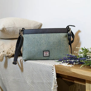 A mint green herringbone Maccessori Harris Tweed Large Shoulder Bag  sitting on top of a side board with flowers to the side. 